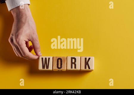 Das Wort ARBEIT ist in Holzwürfeln in schwarzen Buchstaben auf gelbem Hintergrund geschrieben. Stockfoto
