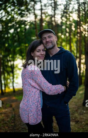 A young Caucasian couple embracing while standing in a lush, green forest Stockfoto