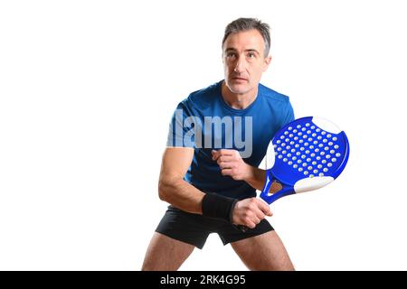 Portrait of man playing padel tennis in position to hit a backhand ball wearing blue and black sports outfit and white isolated background. Front view Stock Photo
