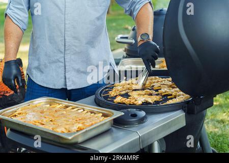 A cook cooks chicken meat on skewers during an outdoor barbecue party in the summer Stock Photo
