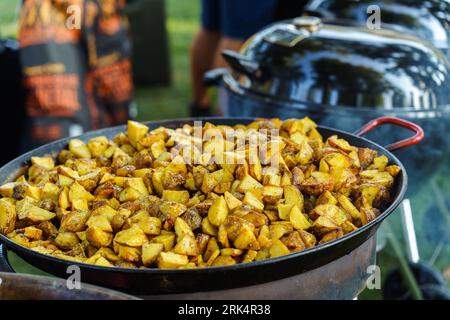 Potatoes are fried in slices in a large pan during a barbecue party in the garden Stock Photo