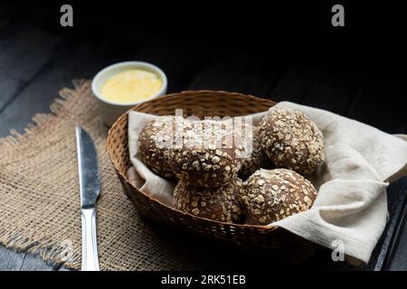 A close-up shot of a rustic basket filled with freshly baked small buns, with a wooden spoon and cloth napkin in the background Stockfoto