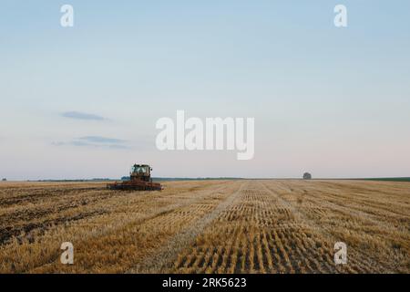 Der moderne Traktor mit einer schweren gezogenen Scheibenegge befährt ein weites hügeliges Feld. Landwirtschaftskampagne im Herbst oder Frühjahr Stockfoto