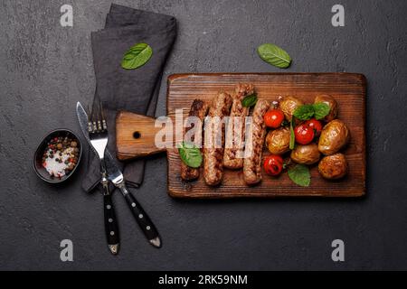 Köstliche gegrillte Würstchen und Kartoffeln auf einem Holzbrett. Flach verlegt Stockfoto