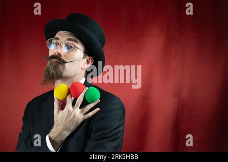 Klassischer kaukasischer Magier mit Hut, Brille und Schnurrbart mit farbigen Kugeln Stockfoto