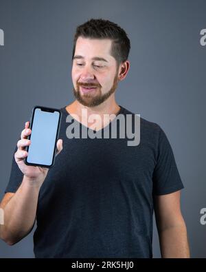 Ein fröhlicher junger Mann, der ein modernes Smartphone in der Hand hält und darauf zeigt, mit Kopierraum Stockfoto