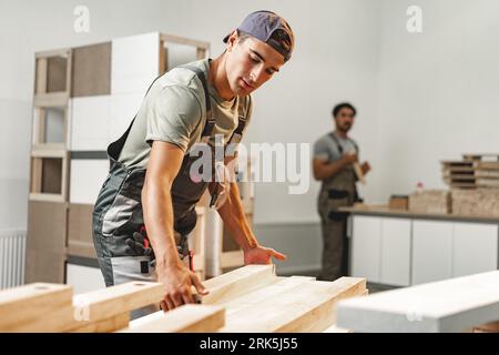 Junger Zimmermann sucht und wählt Holzbohle in einer Werkstatt in einer Holzfabrik Stockfoto