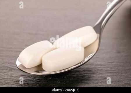 Drei medizinische Pillen mit Metalllöffel auf Schieferstein, Makro. Stockfoto