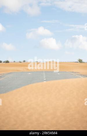 (Selective focus) Stunning view of a deserted road covered by sand dunes. Empty road that run through the Dubai desert. Dubai, United Arab Emirates. Stock Photo