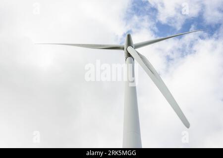 A large wind turbine with white blades on a gray pole isolated on background of the cloudy blue sky Stockfoto