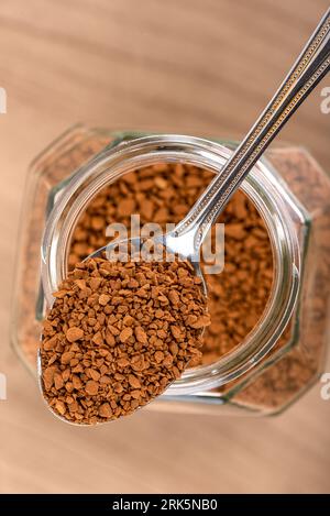 Spoon with instant granulated coffee over a jar on a wooden background. Copy space. Stock Photo