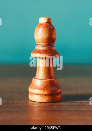 A close-up of a wooden chess pawn on a blue background is in focus Stock Photo