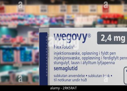 Verpackungskarton mit Wegovy (Semaglutid) injizierbarem verschreibungspflichtigem, gewichtsreduzierendem Arzneimittel von Novo Nordisk A/S. Verschwommene Ladenregale im Hintergrund. Stockfoto