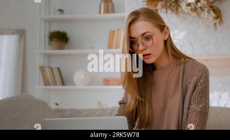 Caucasian shocked woman in glasses looking at laptop reading bad news close mouth with hands holding head with shock failure student girl lost with Stockfoto