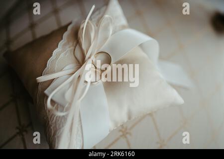 Ein Abschluss aus zwei goldenen Eheringen, die auf einem weißen Satin-Kissen ruhen und mit einer weißen Schleife gebunden sind Stockfoto