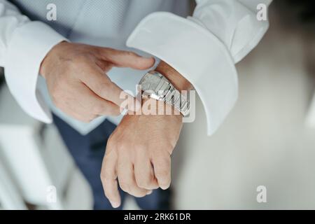 A Caucasian male wearing a crisp white shirt and a modern silver wristwatch is standing in an upright position Stock Photo