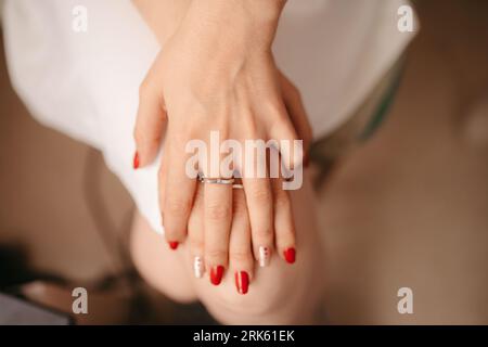 A young woman with an elegant ring on her finger sits comfortably in a relaxed position, her arms resting on her knees Stockfoto