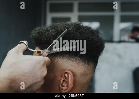 A male barber expertly combs and styles the hair of a customer sitting in a barber chair Stockfoto