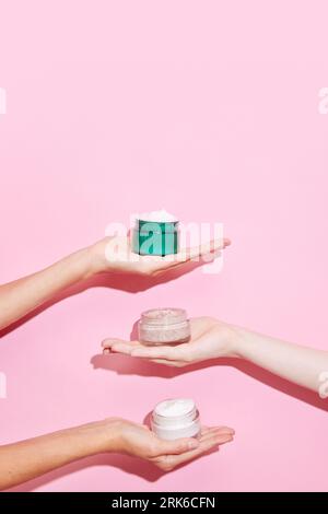 Offene Gläser kosmetischer Cremes mit Frauenhänden auf rosa Hintergrund. Weibliche Gesichtspflege. Anti-Aging. Behandlungen. Stockfoto