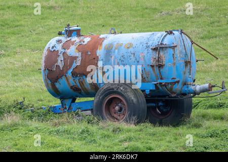 Ein blauer Traktor mit Rostspuren an der Seite, der auf einem Feld vor einer Baumkulisse steht Stockfoto