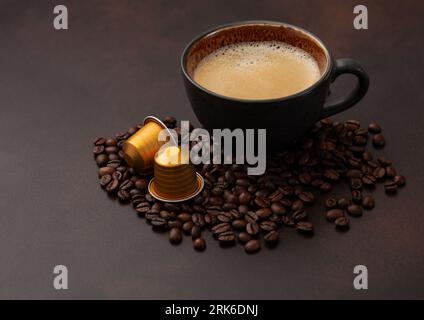 Schwarzer Kaffee in großer Porzellantasse mit rohen Bohnen und Kapseln auf Braun. Stockfoto