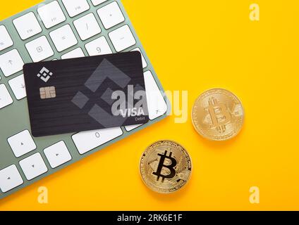 LONDON,UK - NOVEMBER 12, 2022: Binance credit card with two bitcoins and keyboard for cryptocurrency trading market on yellow background. Top view. Stock Photo