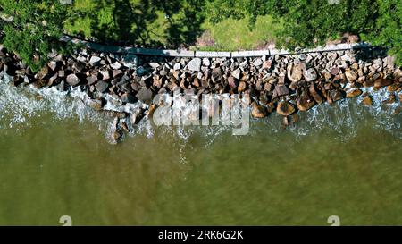 Eine Luftaufnahme der Meereswellen, die gegen eine grüne, felsige Küste prallen Stockfoto