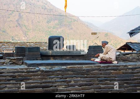 Ein lässig gekleideter Mann sitzt am Rand einer Steinmauer, in seinen Händen in das Buch vertieft Stockfoto