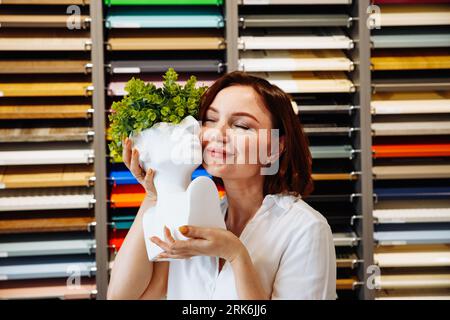 Junge lächelnde Frau, weißer Vasenkopf mit Blättern in den Händen auf bunten Proben stehen an der Wand. 36 Jahre altes weißes Weissweiß-Frauenportrait. Inter Stockfoto