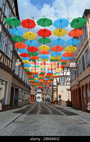 An urban street scene with brightly colored umbrellas suspended over the sidewalk, creating a cheerful atmosphere Stock Photo