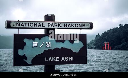 Karte des Ashi-Sees im Hakone-Nationalpark, Japan. Der japanische Text wird als Ashi-See übersetzt. Filter im Retro-Stil, mit See und Torrii-Tor hinter dem Schild. Stockfoto