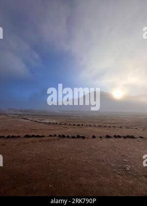 A scenic view of a majestic mountain range in fog illuminated by the golden light of a sun-filled sky Stockfoto