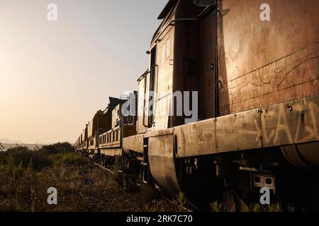 Ein alter, rostiger Zug auf Bahngleisen, umgeben von üppigen grünen Hügeln und Gras Stockfoto