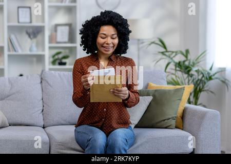 Eine junge afroamerikanische Studentin erhielt die Ergebnisse der Prüfung, des Interviews und der Zulassung zur Universität. Er liest den erhaltenen Brief, der zu Hause auf dem Sofa sitzt. Stockfoto