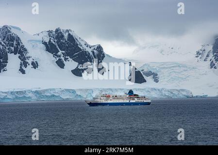 Ein großes Segelboot, das vor einer atemberaubenden Kulisse aus verschneiten Berggebieten in der Antarktis abgebildet ist Stockfoto