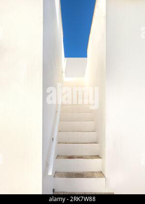 Eine Treppe mit weißen Wänden führt zu einem hellblauen Himmel Stockfoto