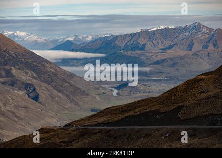 This breathtaking view showcases a long, winding road stretching out in the foreground and leading to a range of majestic snow-tipped mountains Stock Photo