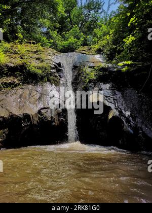 An image of a serene waterfall cascading down a majestic rocky face into a rushing river below Stock Photo