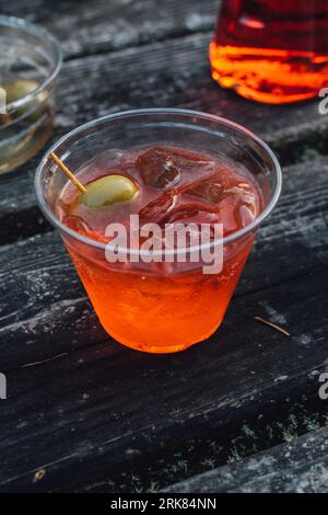 Glamping with a aperol spritz aperitif cocktail happy hour outdoors in plastic cup on wooden picnic table Stock Photo