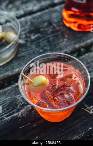 Glamping with a aperol spritz aperitif cocktail happy hour outdoors in plastic cup on wooden picnic table Stock Photo