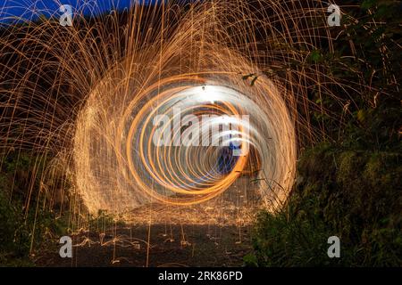 Eine nächtliche Szene, in der ein brennendes Feuer durch sich drehende Stahlwolle mit einer langen Belichtung entsteht. Stockfoto