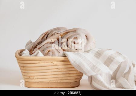 Ein weißer Tisch mit einem gewebten Korb mit einer Auswahl frisch gebackener Brötchen, bedeckt mit einem gemusterten Tuch, um sie warm zu halten Stockfoto