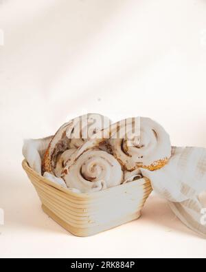 A closeup of a basket of freshly-baked cinnamon rolls nestled next to a flaky pastry on a white cloth napkin Stock Photo