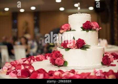 Dieses Bild zeigt eine atemberaubende dreistufige weiße Hochzeitstorte, die auf einem weißen Tisch ruht Stockfoto
