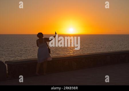Silhouette einer Frau nahm sich selbst ein Selfie gegen die Sonne während des Sonnenuntergangs in Maspalomas, Gran Canaria, Spanien Stockfoto