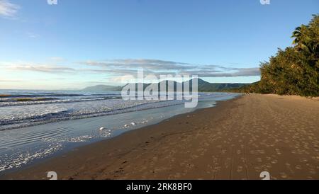 An expansive view of an empty beach with the glistening waves of the ocean washing up onto the shoreline Stock Photo