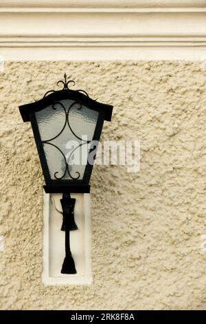 Alte schwarze Straßenlaterne auf gelber Gipswand bei Tageslicht Stockfoto