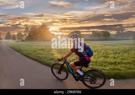 Nette Frau mit E-Mountainbike, Radfahren im stimmungsvollen Morgenlicht auf dem Neckartalradweg bei Ludwigsburg, Baden Württemberg, Deutschland Stockfoto