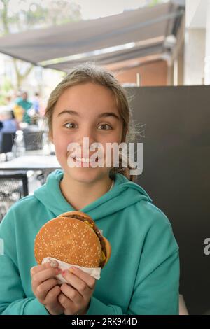 Girl in a cafe with a big hamburger. Fast food, lifestyle. Portrait Close-up. Place for text Stock Photo