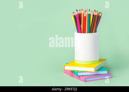 Buntstifte in weißem Glas und Notizbüchern mit Platz für Text auf grünem Hintergrund. „Back to School“-Konzept Stockfoto